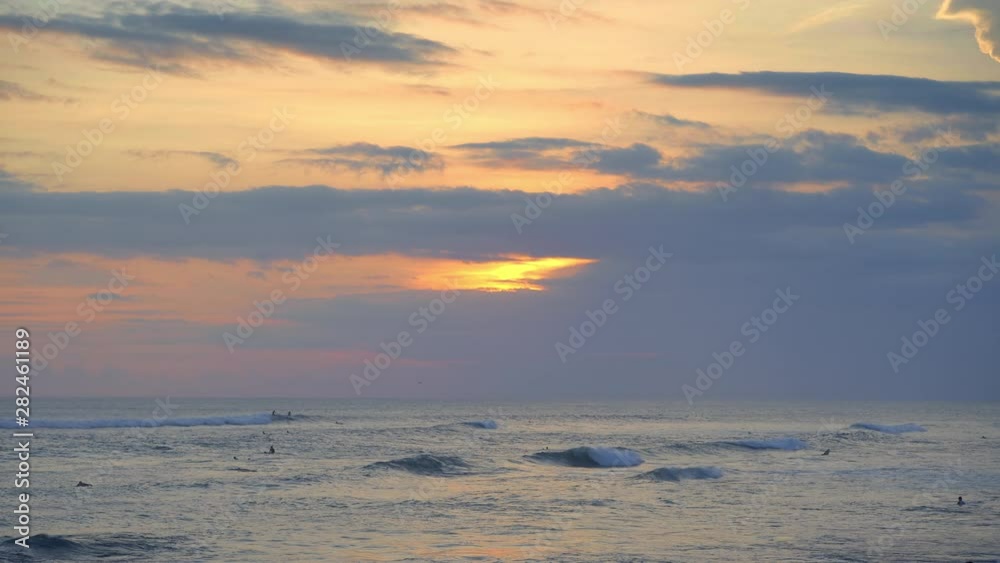 Surfers are swimming in warm ocean with big blue waves during beautiful sunset in Bali island Surfers are swimming in warm ocean with big blue waves during beautiful sunset in Bali island