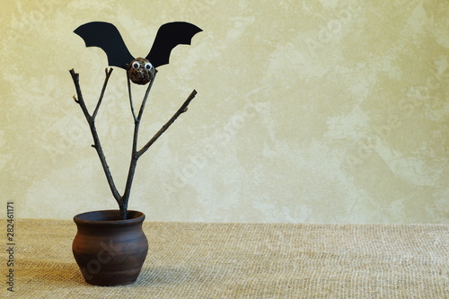 Tableau sur toile Old dry branch and bat from fir cone and black cardboard in clay vase on homespun jute fabric against light wall