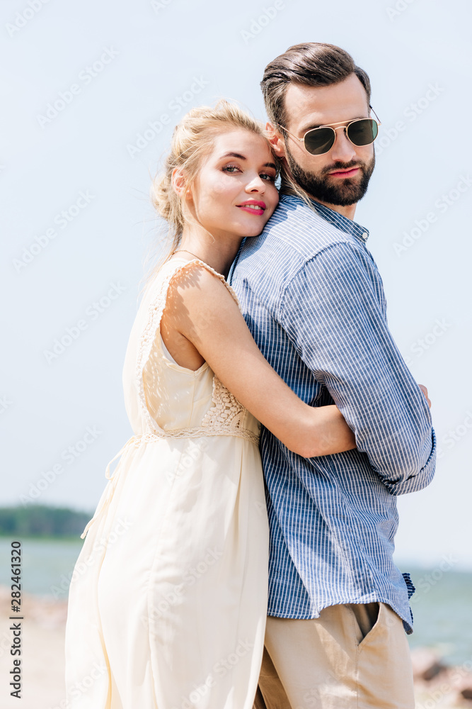 low angle view of happy blonde woman hugging bearded boyfriend at beach low angle view of happy blonde woman hugging bearded boyfriend at beach