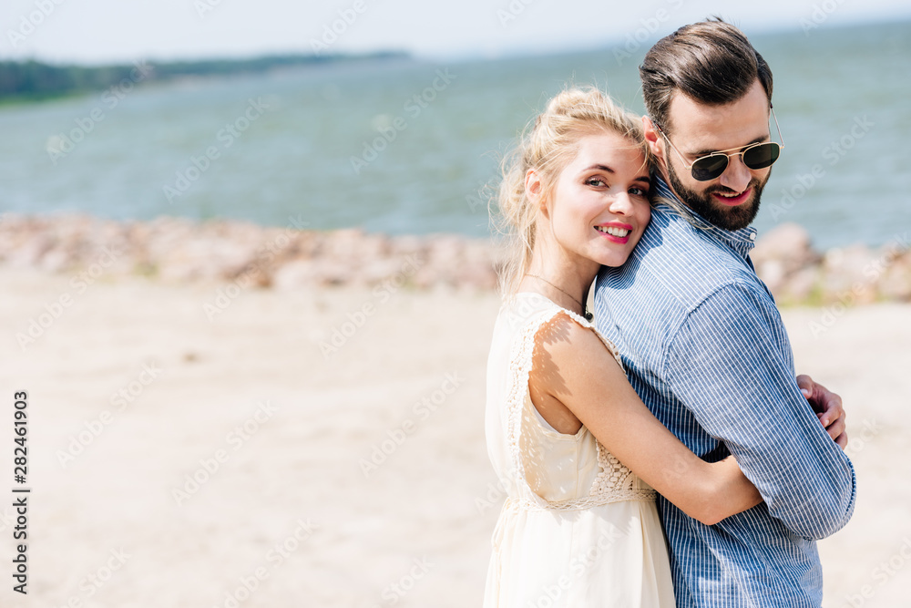 happy blonde woman hugging bearded smiling boyfriend at beach happy blonde woman hugging bearded smiling boyfriend at beach