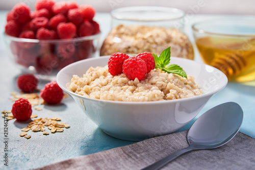 Homemade oatmeal with fresh raspberries and organic honey for breakfast on a turquoise background.