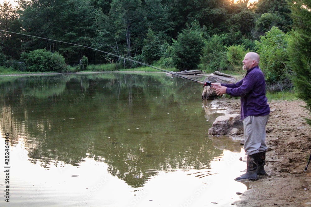 Peaceful Scene of Middle Aged Man Fishing on a Country Pond at Sunset with Golden filtered light reflected on pond Peaceful Scene of Middle Aged Man Fishing on a Country Pond at Sunset with Golden filtered light reflected on pond