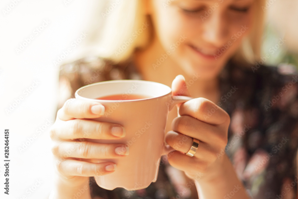 Close up photo of pretty woman holding mug of delicious hot tea, drinking, smiling, in cozy morning cafe, selective focus, noise effect Close up photo of pretty woman holding mug of delicious hot tea, drinking, smiling, in cozy morning cafe, selective focus, noise effect