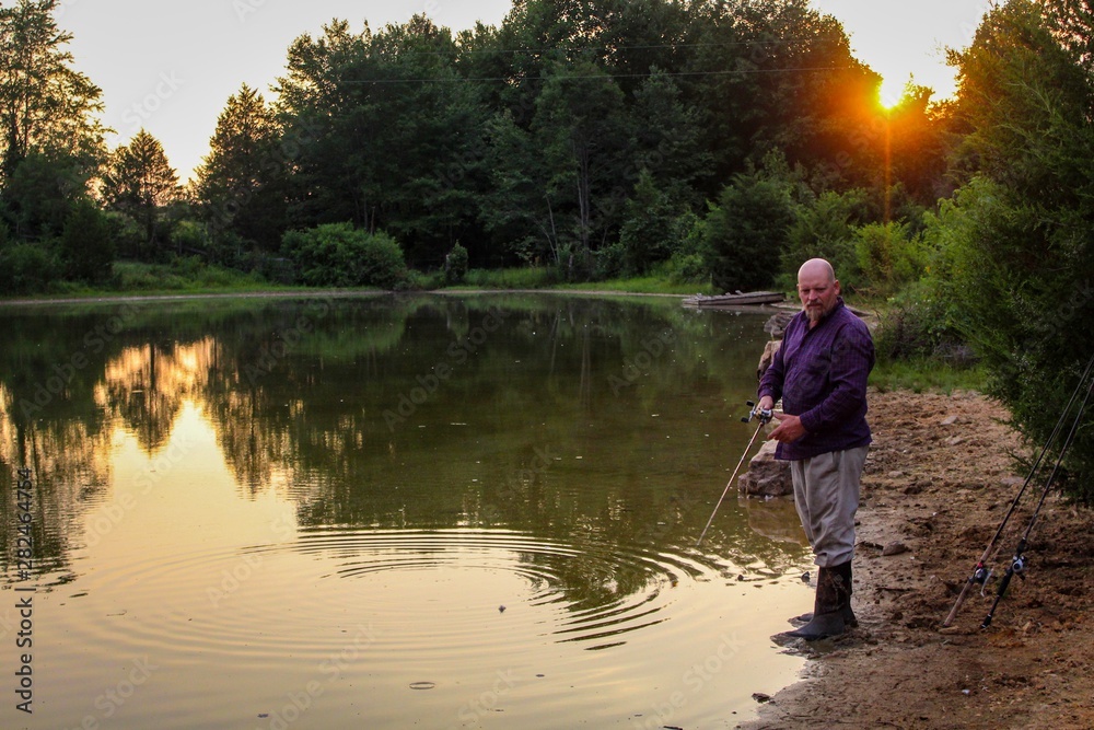 Peaceful Scene of Middle Aged Man Fishing on a Country Pond at Sunset with Golden filtered light reflected on pond Peaceful Scene of Middle Aged Man Fishing on a Country Pond at Sunset with Golden filtered light reflected on pond
