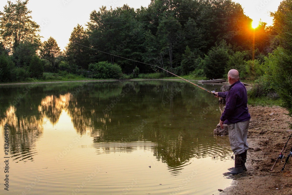 Peaceful Scene of Middle Aged Man Fishing on a Country Pond at Sunset with Golden filtered light reflected on pond Peaceful Scene of Middle Aged Man Fishing on a Country Pond at Sunset with Golden filtered light reflected on pond