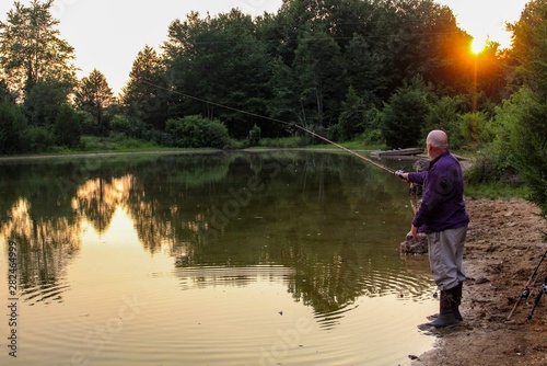 Peaceful Scene of Middle Aged Man Fishing on a Country Pond at Sunset with Golden filtered light reflected on pond