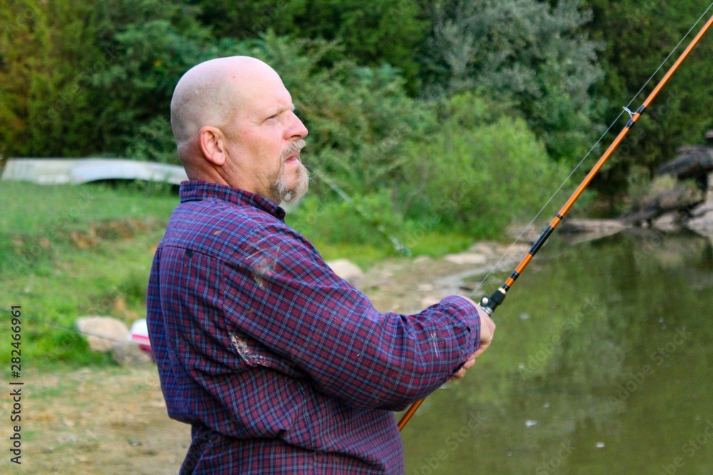 Peaceful Scene of Middle Aged Man Fishing on a Country Pond at Sunset with Golden filtered light reflected on pond Peaceful Scene of Middle Aged Man Fishing on a Country Pond at Sunset with Golden filtered light reflected on pond
