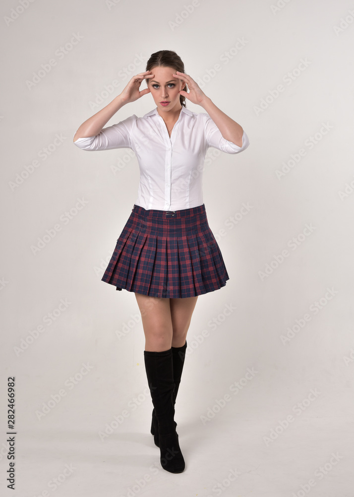 full length portrait of a brunette girl wearing a white shirt and plaid skirt uniform, standing pose against a cream studio background. full length portrait of a brunette girl wearing a white shirt and plaid skirt uniform, standing pose against a cream studio background.