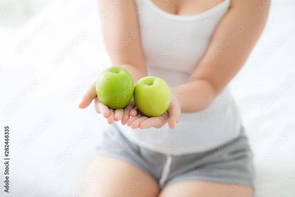 Closeup young asian woman holding and eating green apple fruit in the bedroom at home, lifestyle of nutrition girl healthy and care weight loss, health and wellness concept.