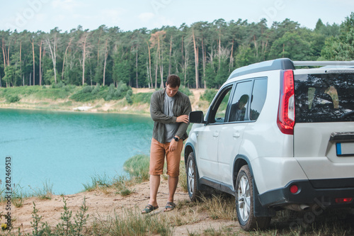 man near white suv car at the edge looking at lake with blue water