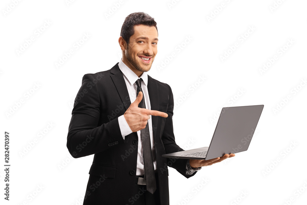 Young professional man in a suit holding a laptop and pointing at it Young professional man in a suit holding a laptop and pointing at it