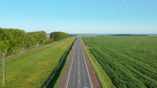 Road between fields and forest belt.Cars driving on the road and overtaking.Asphalt road in Russia.Aerial pull away shot.