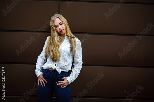 Portrait of a young cute caucasian girl with problem skin in white shirt opposite brown background on the street in spring.