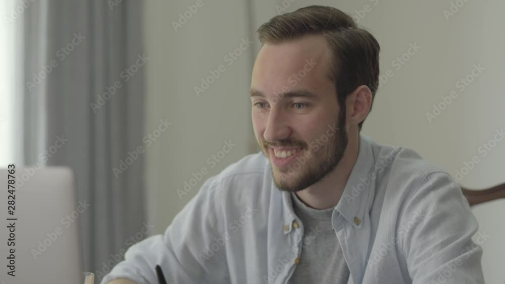 Portrait of a young handsome man smiling and nodding sitting in front of his computer in the office. The office worker got good news, the guy in a good mood at work. Real people series. Portrait of a young handsome man smiling and nodding sitting in front of his computer in the office. The office worker got good news, the guy in a good mood at work. Real people series.