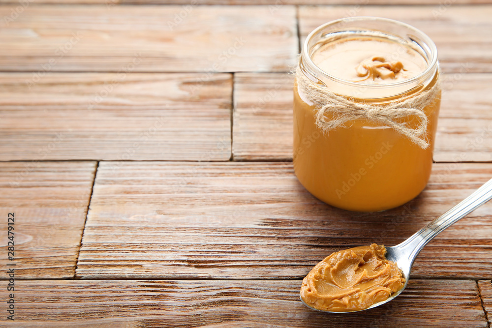 Peanut butter in glass jar with spoon on brown wooden table