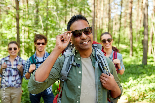 travel, tourism, hike and people concept - man in sunglasses and group of friends with backpacks in forest