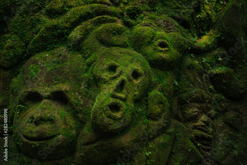 Carving demons faces on wall background covered with moss texture in Bali