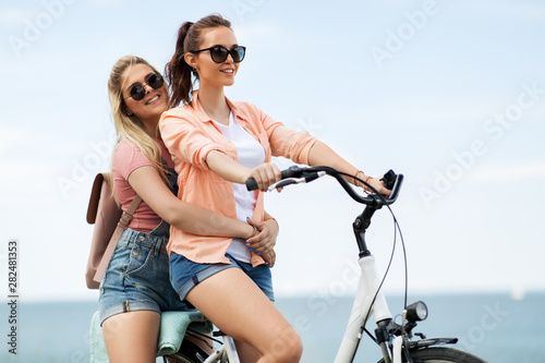 leisure and friendship concept - happy smiling teenage girls or friends riding bicycle together at seaside in summer © Syda Productions