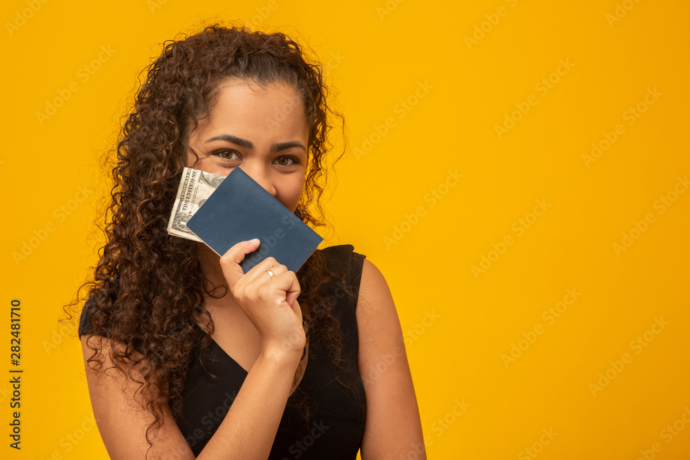 Beautiful young woman with curly hair holding a passport and money, thinking of her next trip. On yellow background Beautiful young woman with curly hair holding a passport and money, thinking of her next trip. On yellow background