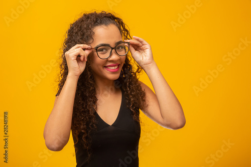 Beautiful young woman with curly hair happy with her glasses. Eye care concept. On yellow background