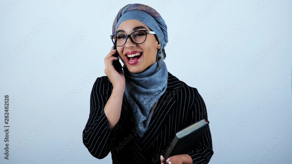 young beautiful arabic business woman wearing eyeglasses holding planner having successful conversation on smartphone feeling happy on isolated white background young beautiful arabic business woman wearing eyeglasses holding planner having successful conversation on smartphone feeling happy on isolated white background