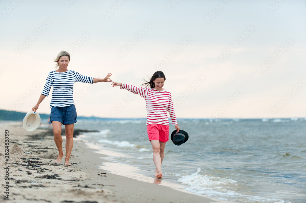 Two young women walking together on the seaside holding hands