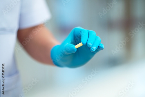 The doctor wears blue gloves  holding yellow capsules.