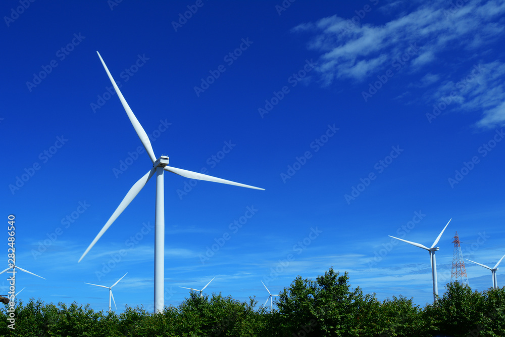 The white electric wind turbine with blue sky and trees at Petchaboon,Thailand The white electric wind turbine with blue sky and trees at Petchaboon,Thailand