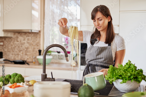 Smiling Caucacian brunette in apron standing in kitchen and preparing spaghetti. Italian food preparation concept. photo