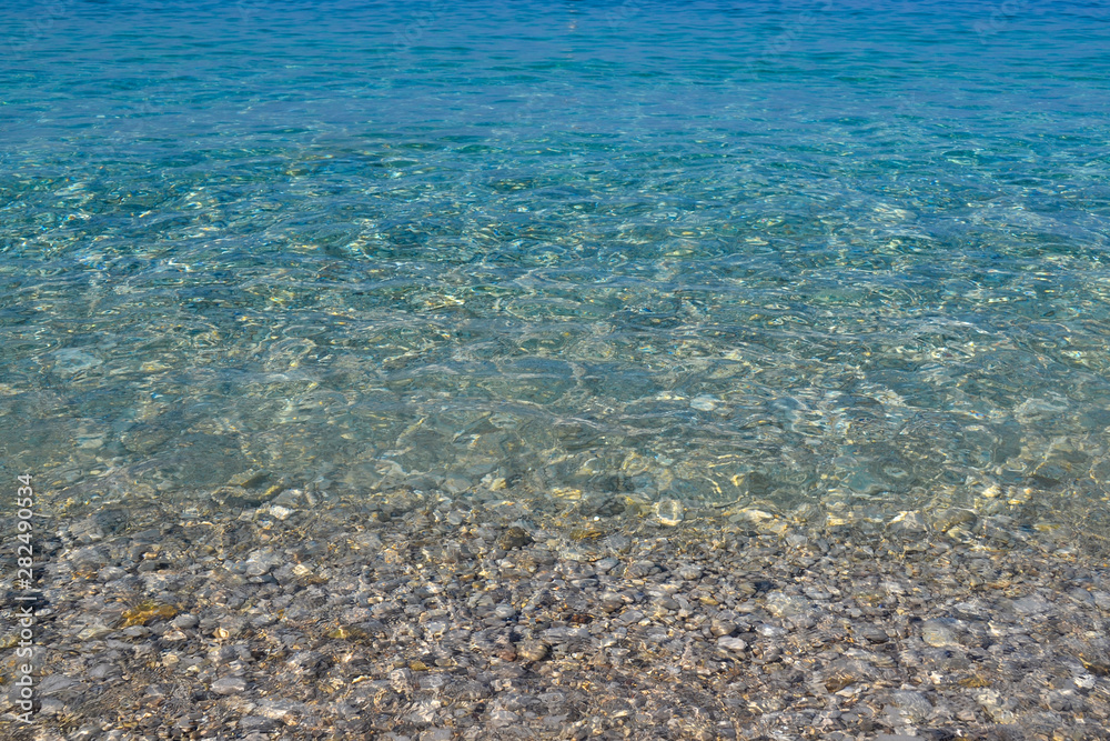 Obraz premium square background image of calm turquoise sea on shingle beach