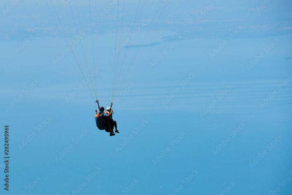 Fototapeta premium Paraglider flying over the Garda Lake (Lago di Garda or Lago Benaco), Panorama of the gorgeous Garda lake surrounded by mountains. Paragliding is very popular sport in Monte Baldo. Malcesine, Italy