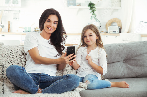 Smiling mother and little daughter playing games with smartphone