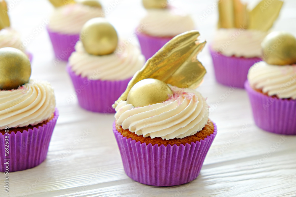 Sweet organic cupcake in purple wrap with cream cheese frosting swirl and golden chocolate decoration on white wooden textured table. Close up, copy space, background.