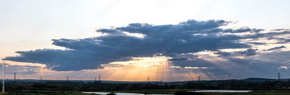 Naklejka premium Panorama Sunset - Sun Hiding Behind Dark Clouds Creating God Rays