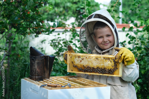 Cheerful boy beekeeper in protective suit near beehive. Honeycomb with honey. Organic food concept. The most useful organic honey. photo