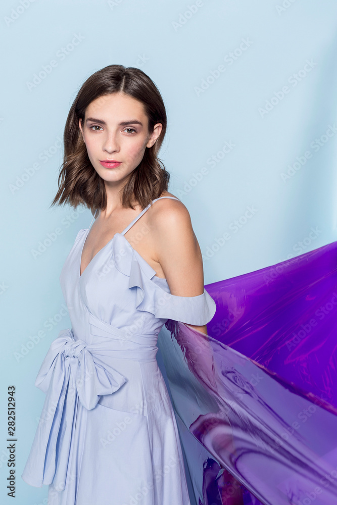 Portrait of a female fashion model posing with purple plastic sheet against blue background Portrait of a female fashion model posing with purple plastic sheet against blue background