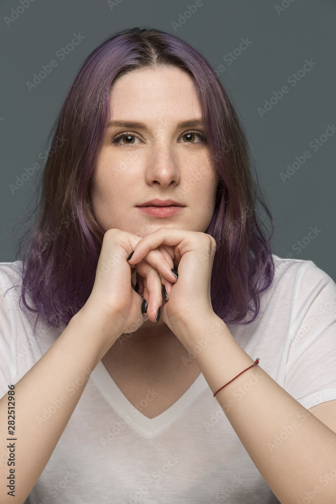 Portrait of a young woman with dyed hair and resting chin on hands against gray background Portrait of a young woman with dyed hair and resting chin on hands against gray background