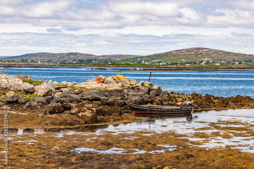 Bay with low tide, seaweeds, boat and mountains in Carraroe
