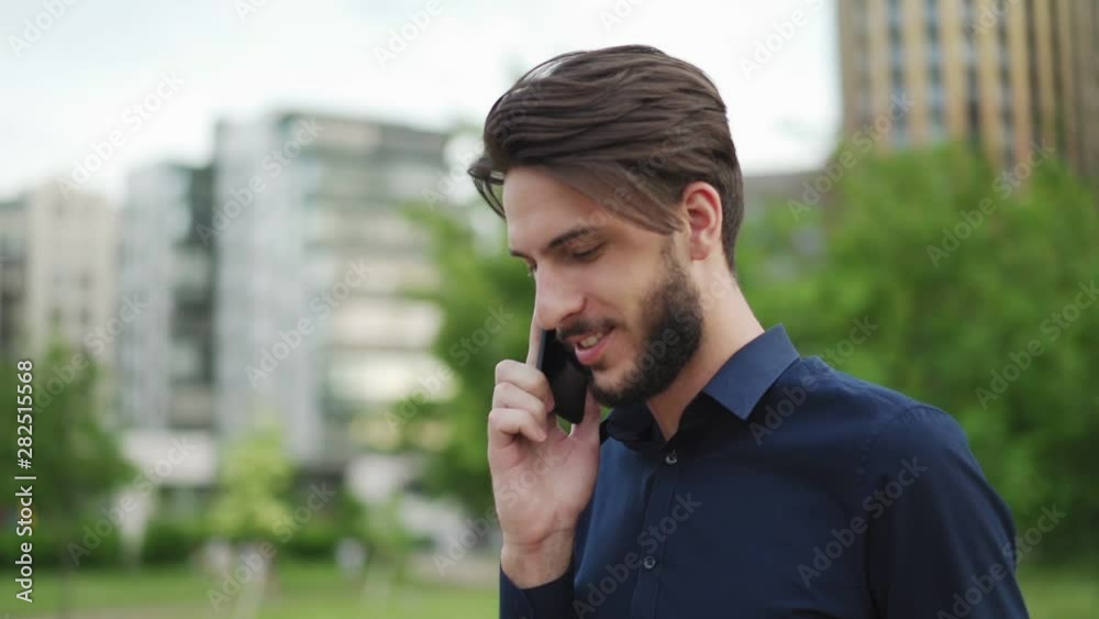 Panning slow motion shot of smiling young businessman with beard talking on cell phone while walking down city street Panning slow motion shot of smiling young businessman with beard talking on cell phone while walking down city street