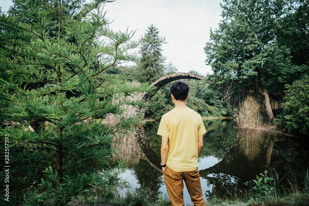 Teenage boy looking at tranquil Rakotzbruecke Devils Bridge, Rakotzbruecke, Brandenburg, Germany Teenage boy looking at tranquil Rakotzbruecke Devils Bridge, Rakotzbruecke, Brandenburg, Germany