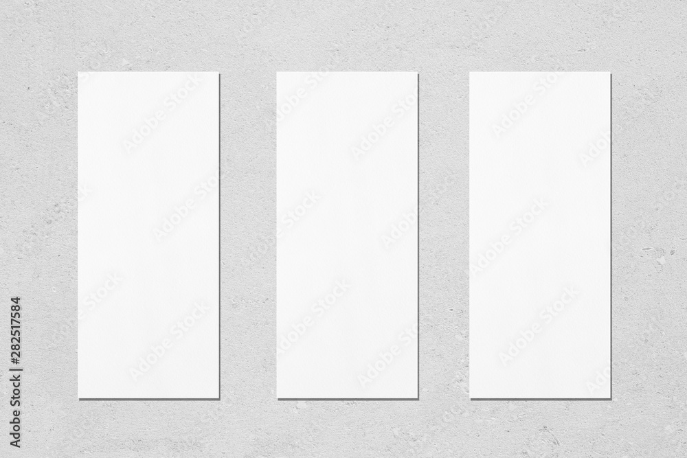 Three empty white vertical rectangle poster menu mockups with soft shadows on neutral light grey concrete wall background. Flat lay, top view - obrazy, fototapety, plakaty 