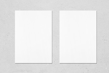 Two empty white vertical rectangle poster mockups with soft shadows on neutral light grey concrete wall background. Flat lay, top view