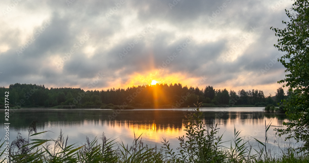 Orange-yellow sunrise through a strong cloud over the lake Orange-yellow sunrise through a strong cloud over the lake