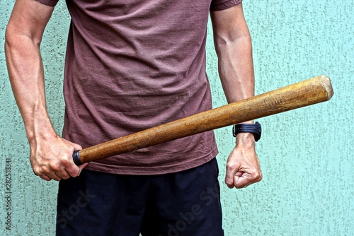 wooden bat in a man’s hand against a gray wall