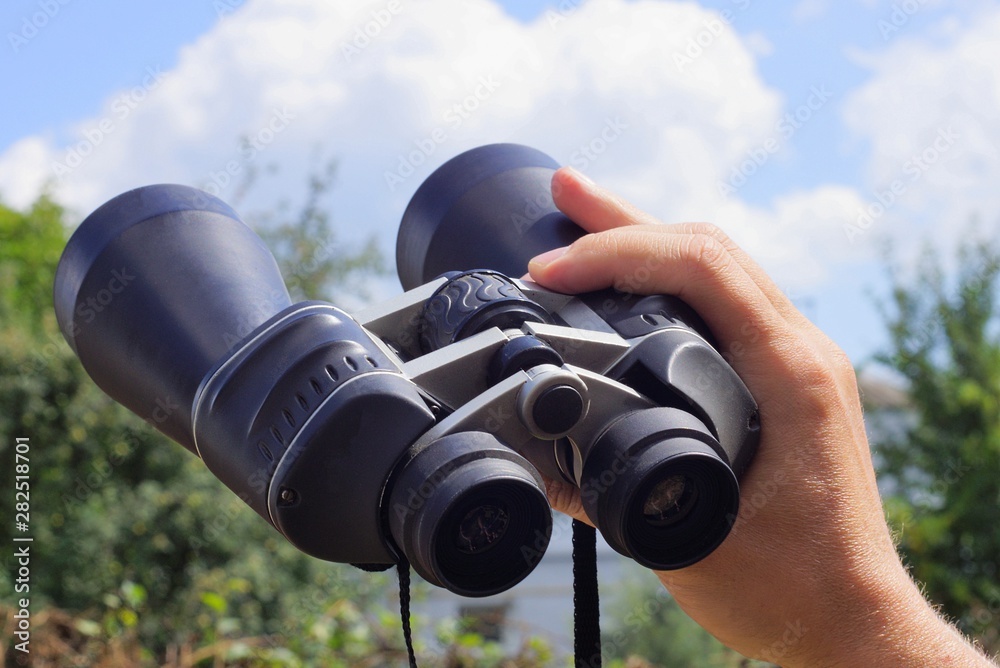hand holds big black binoculars against the sky and clouds
