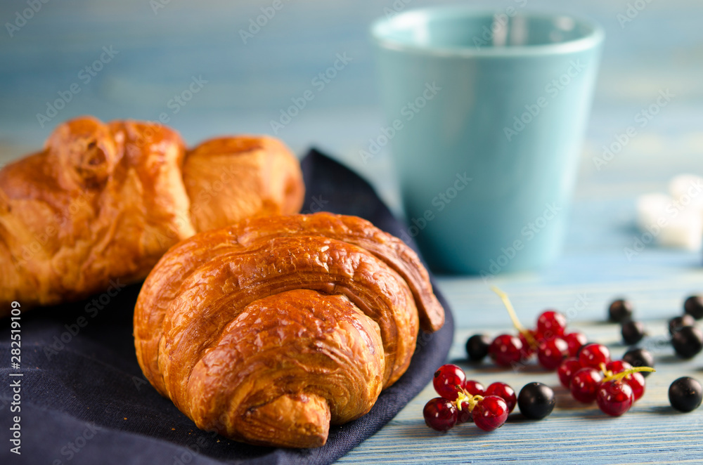 Fresh ruddy croissants with berries lie on a wooden table next to fresh black currant berries, red currants Fresh ruddy croissants with berries lie on a wooden table next to fresh black currant berries, red currants