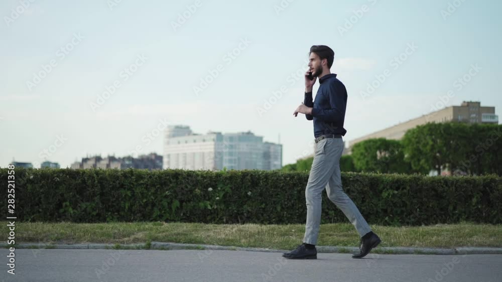 Tracking slow motion shot of displeased and irritated young businessman scolding on cell phone while walking down street, side view zoom in Tracking slow motion shot of displeased and irritated young businessman scolding on cell phone while walking down street, side view zoom in