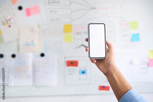 Male hand holding aloft a smartphone in front of a whiteboard