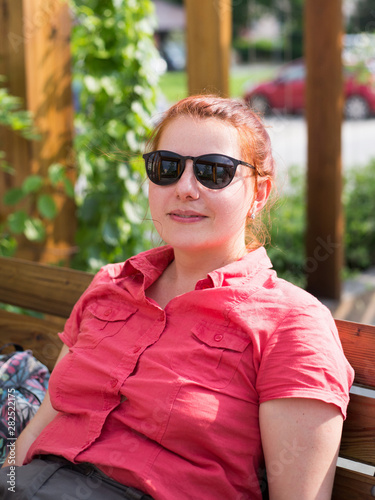 Beautiful young woman with red hair sitting on a bench in a city park, girl relaxed