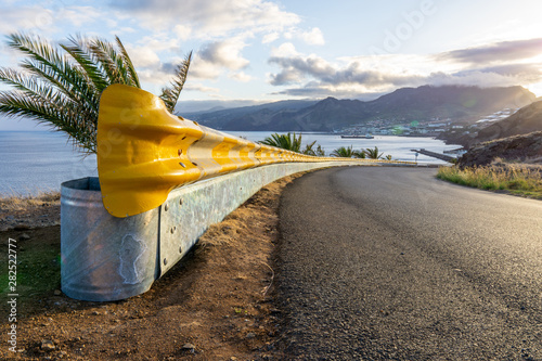 Yellow guardrail along curvy road with sunset over the sea and village